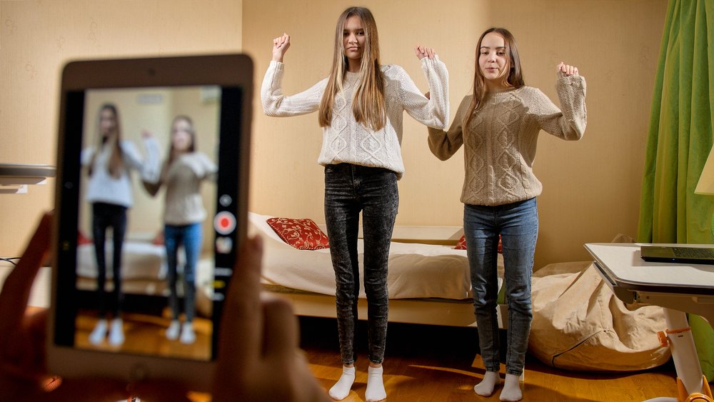 Recording video on a smartphone of two teenage girls dancing for posting on the internet. Modern communication, social media, and gadgets.