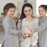 A single mother and her two daughters holding a piggy bank, demonstrating how to save money.